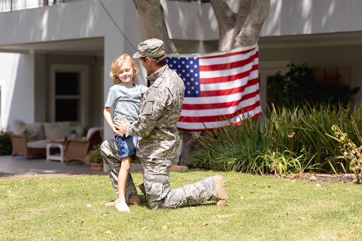 An active-duty Army serviceman hugs his daughter in front of the home he purchased with a credit union mortgage loan.